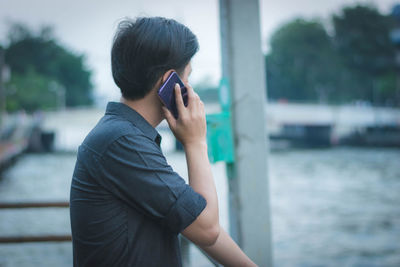 Man talking on mobile phone against pond