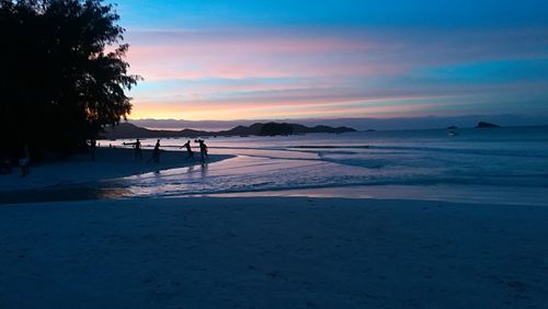 Silhouette people at beach against sky during sunset