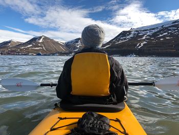 Rear view of man sitting in canoe on river