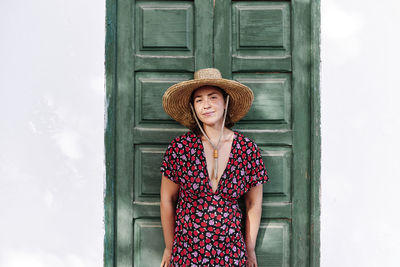 Smiling woman wearing sun hat while leaning on door