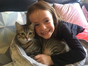 Portrait of girl with cat lying on bed at home