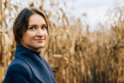 Portrait of confident smiling young short-haired woman in autumn in the middle of a cornfield