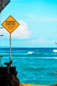 Close-up of warning sign by sea against sky