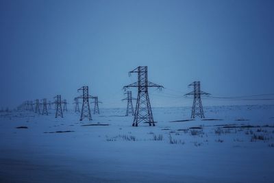 Electricity pylon on snowy ground against an evening blue sky