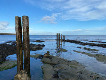 Wooden posts in sea against sky