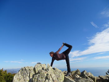 Low angle view of person standing on rock against sky