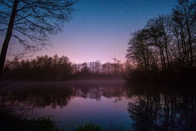 Reflection of silhouette trees in lake against sky at night