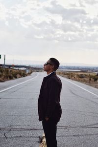 Young man standing on road against sky