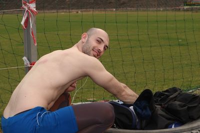 Portrait of shirtless man listening music while crouching on field