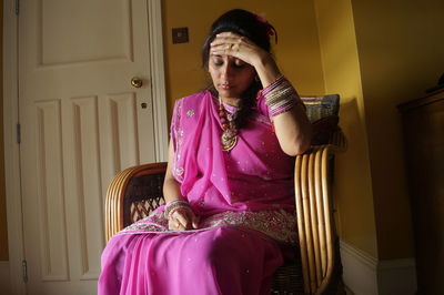 Woman with headache sitting in pink sari on chair at home