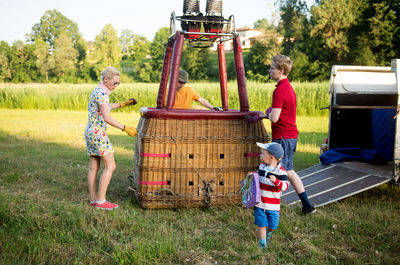 Pilot with people preparing hot air balloon on grassy field during sunset