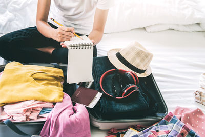 Midsection of woman packing luggage while sitting on bed at home