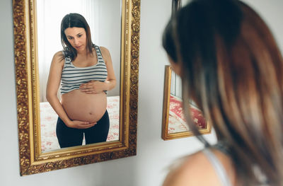 Pregnant woman looking in mirror at home