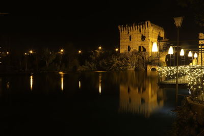 Illuminated buildings by lake against sky in city at night