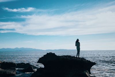 Man standing on rock by sea against sky