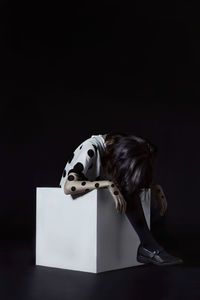 Side view of woman sitting against black background