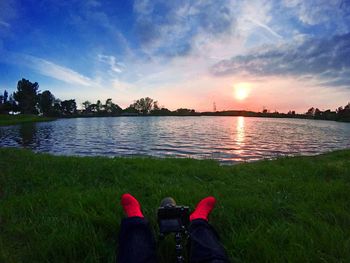 Low section of man on lake against sky during sunset