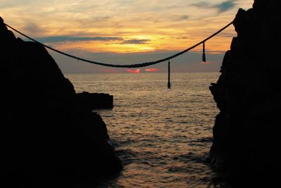 Silhouette rocks on beach against sky during sunset