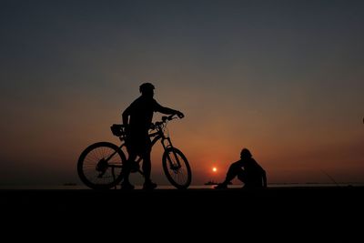 Silhouette man with bicycle against sea and sky during sunset