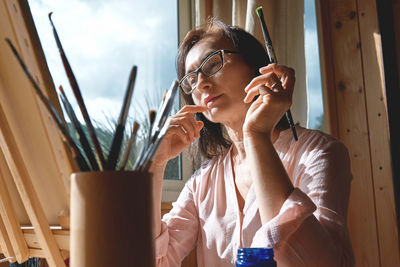 Concentrated woman painting picture on canvas at easel near the window in the studio. 