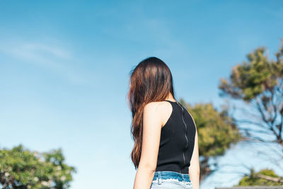 Rear view of woman standing against blue sky during sunny day