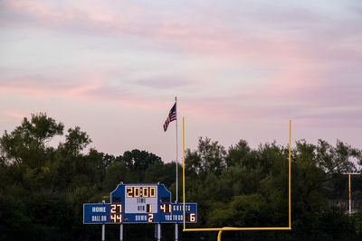 Illuminated scoreboard by flag against trees