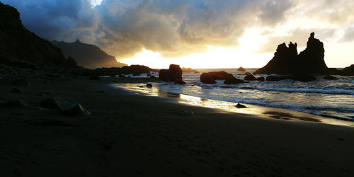 Silhouette beach by sea against sky during sunset