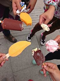 Cropped image of friends holding ice cream on footpath