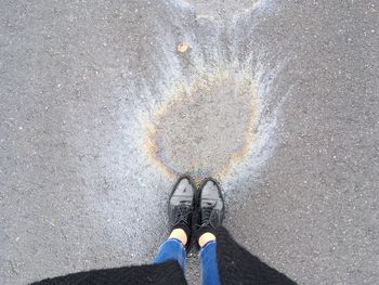 Low section of woman standing by oil spill on road