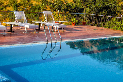 Empty chairs by swimming pool against trees