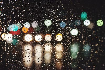 Illuminated cars seen through wet glass window at night during monsoon