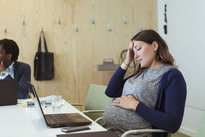 Tired pregnant professional looking at laptop in office meeting