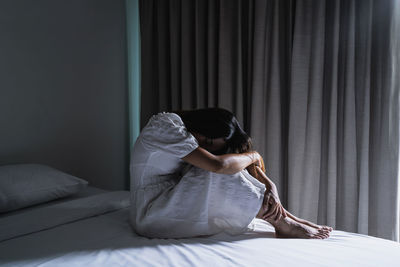 Full length of depressed woman sitting on bed