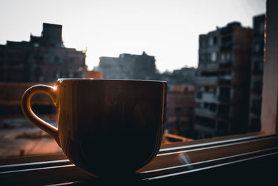 Close-up of coffee cup against window in city