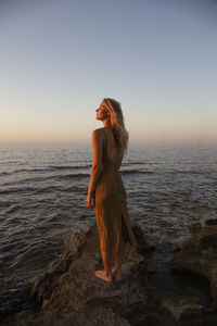 Woman standing on beach against sky during sunset