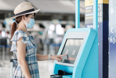 Side view of woman wearing mask standing by ticket machine