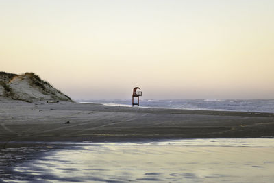 Man standing on beach against clear sky during sunset