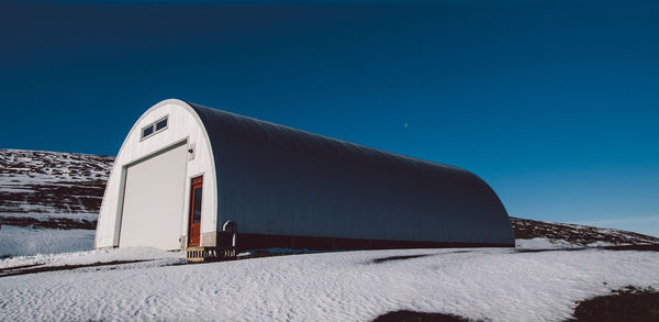 Built structure on snow covered land against clear blue sky