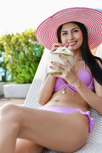 Seductive woman wearing bikini drinking coconut water on lounge chair