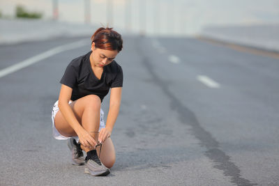 Young woman tying shoelace on road