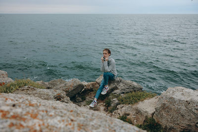 Woman sitting on rock by sea