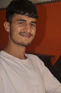 Close-up of a good looking indian young guy smiling, sitting indoors with looking at camera