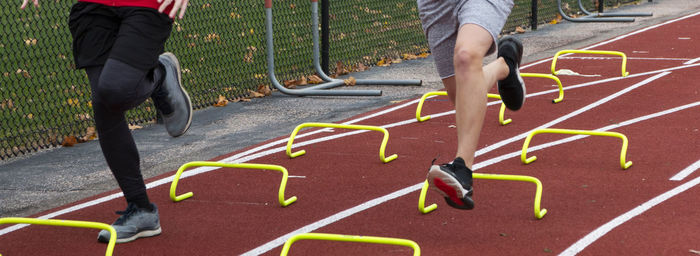 Two boys running over yellow mini hurdles on a red track during track and field practice outdoors.