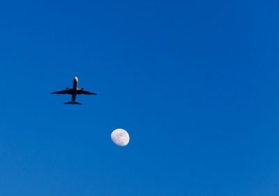 Low angle view of airplane flying against clear blue sky