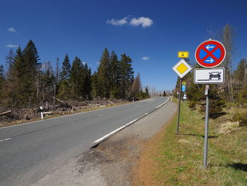 Road sign by trees against sky