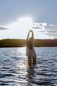 Rear view of woman with arms raised standing in lake against sky