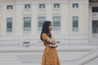 Woman looking away while standing against building