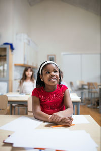 Smiling girl listening while sitting at desk in classroom