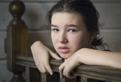 Portrait of depressed girl leaning on wooden railing at home