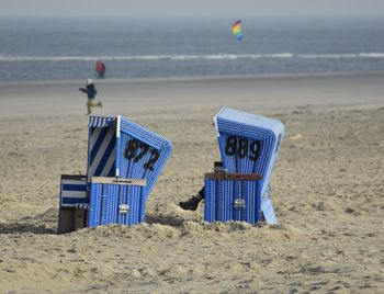 Hooded chairs on sand at beach against sky